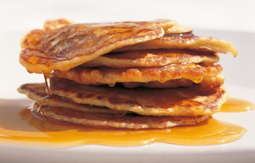 Pouring a thick homemade Maple Syrup Substitute over pancakes A pitcher pouring a thick, golden brown homemade maple syrup substitute over a stack of pancakes