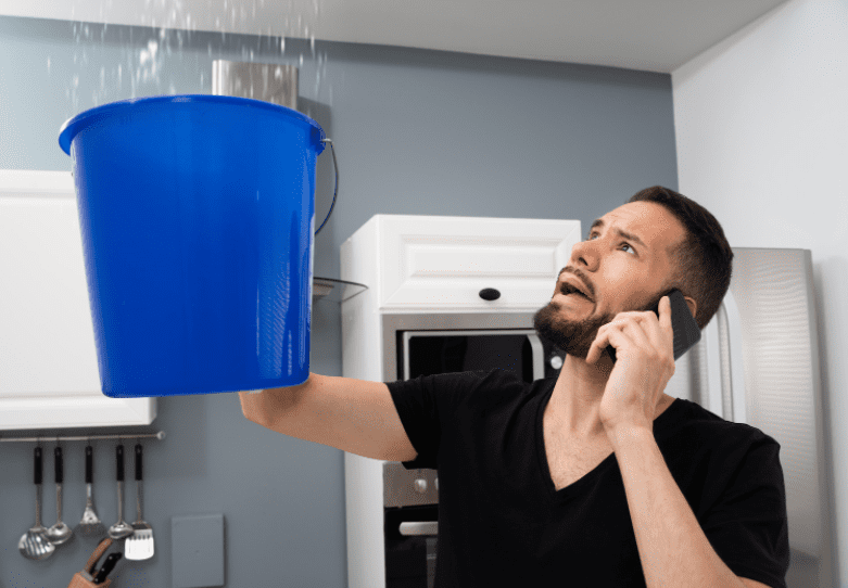 How To Repair A Leaking Ceiling A homeowner inspecting a severe water leak and bubbling paint on a living room ceiling.