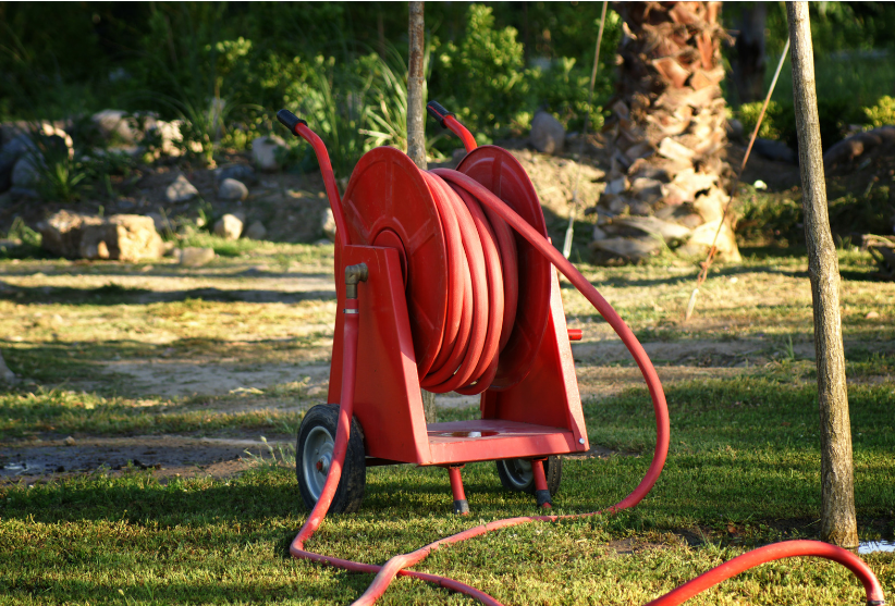 A green retractable garden hose reel mounted on a brick wall.