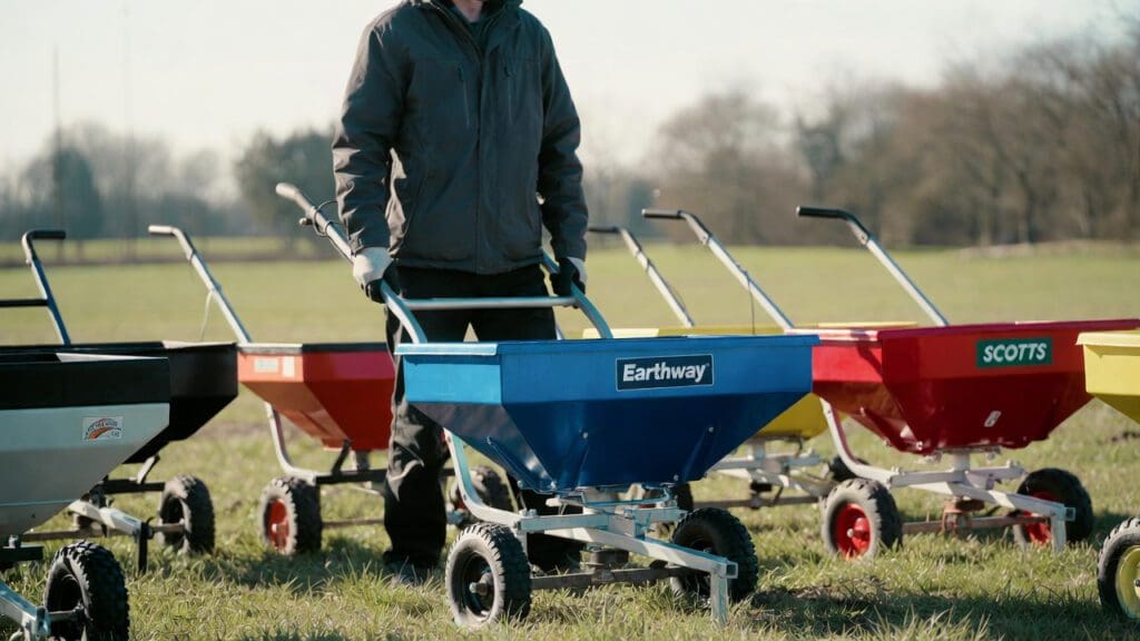 A close-up photograph of three premium broadcast fertilizer and seed spreaders actively working in motion on a lush suburban lawn, representing the hands-on testing of top models for a 2026 article review on gardenfrontier.com.