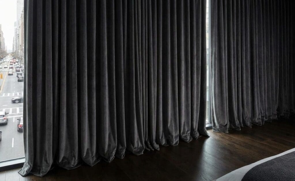 Thick, heavy-duty soundproof curtains installed over a large bedroom window to block street noise