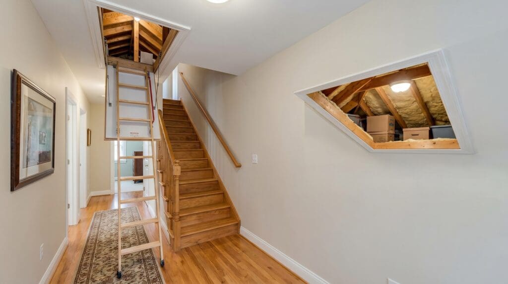 A white attic access door in a hallway ceiling with pull-down attic stairs partially opened